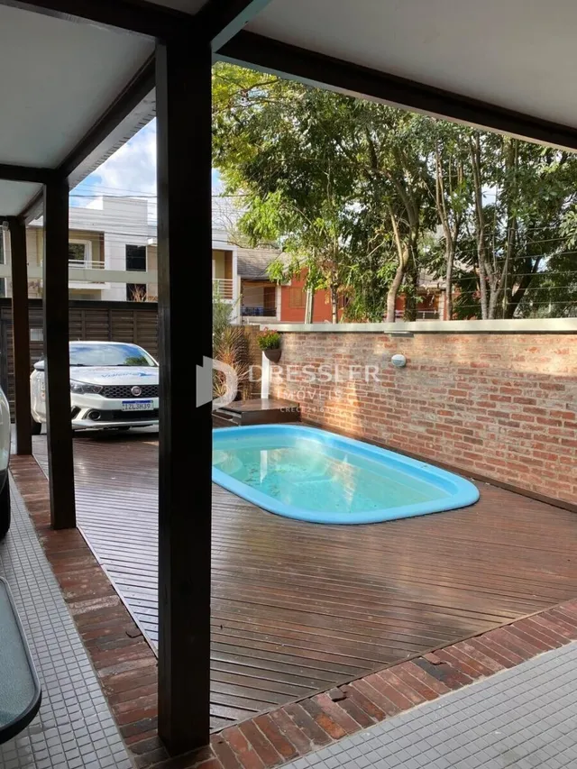 Piscina externa com deck de madeira e parede de tijolos.