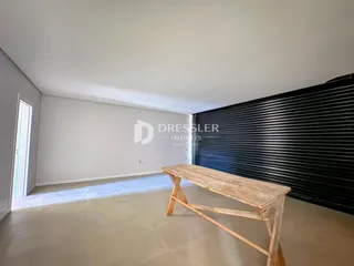 Ambiente interno de uma sala ampla com paredes brancas e piso claro.