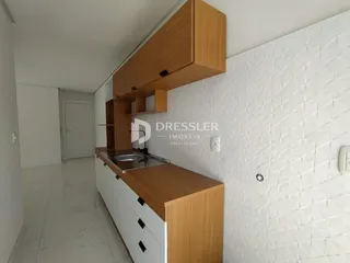 Vista interna de uma cozinha com armários de madeira e revestimento branco.