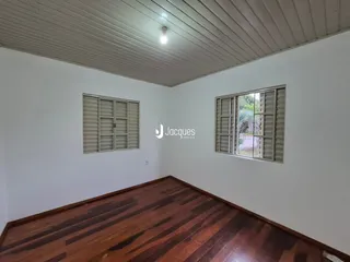 A sala apresenta piso de madeira escura e paredes brancas com duas janelas.