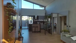 Sala de estar com piso de madeira e grandes janelas no interior de uma residência.