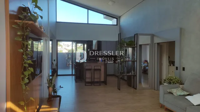 Sala de estar com piso de madeira e grandes janelas no interior de uma residência.