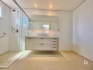 Banheiro moderno com box de vidro e bancada de madeira clara.