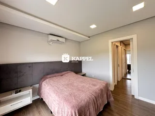 Quarto com cama grande e cabeceira cinza em um ambiente claro.