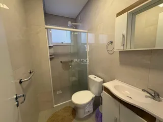 Foto interna de um banheiro com box de vidro e azulejos brancos.