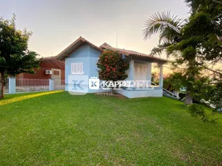Fachada de uma residência com gramado verde e vegetação tropical.