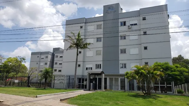 Fachada de um prédio residencial em Lajeado, Brasil, com gramado e árvores no primeiro plano.
