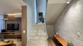 Vista de uma sala de estar com escadaria e parede de tijolos expostos.