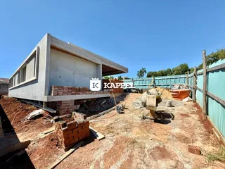Foto da construção de uma casa em um terreno com cerca verde ao fundo.