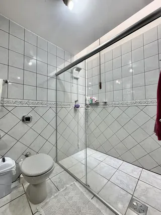 Foto de um banheiro com revestimento cerâmico e box de vidro.