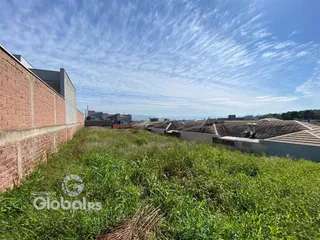 Vista externa de uma propriedade com muro de tijolos e gramado alto.