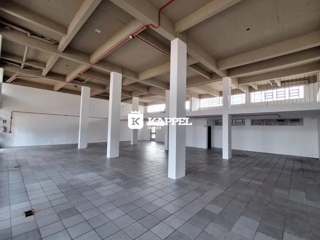 Vista interna de um espaço amplo com colunas brancas e piso de cerâmica.