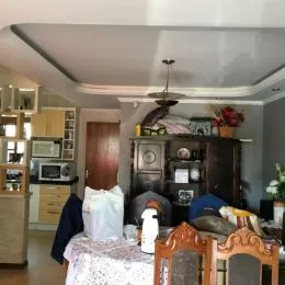 Sala de estar com móveis de madeira escura e cortinas brancas.