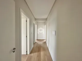 Corredor interno de uma residência com piso de madeira clara e paredes brancas.