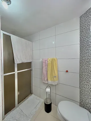 Banheiro com revestimento de azulejos brancos e toalhas penduradas.