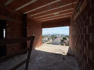 Vista interna de um corredor com paredes de tijolo aparente e acesso a um terreno externo.