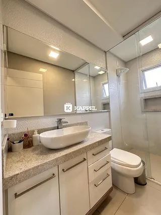 Banheiro com bancada de granito e box de vidro transparente.