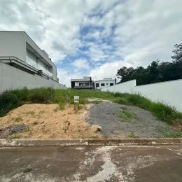 Vista externa de um terreno com vegetação rasteira e muro branco ao fundo.
