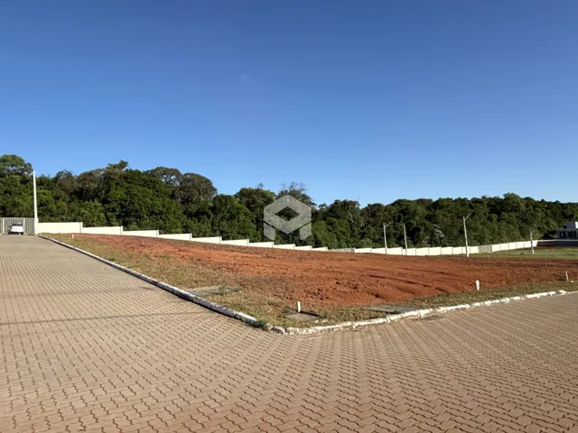 Vista da divisa de uma propriedade com terra avermelhada e vegetação ao fundo.