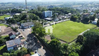 Vista aérea de um terreno com um campo gramado cercado por árvores e construções.