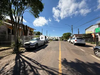 Vista externa de uma rua em Lajeado, Brasil, com veículos estacionados e vegetação ao lado.