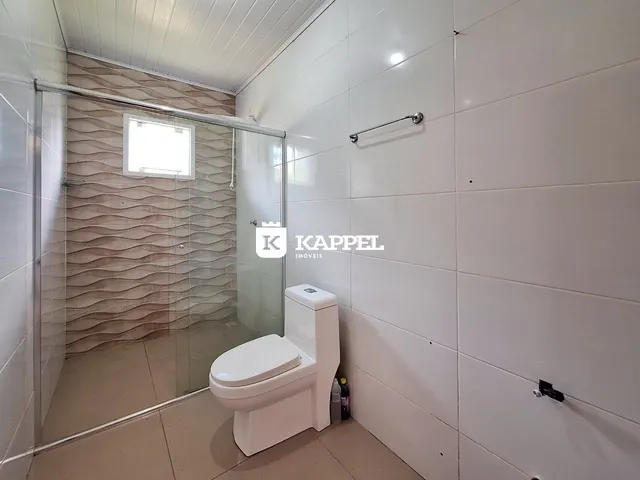 Banheiro com revestimento de azulejos claros e box de vidro transparente.