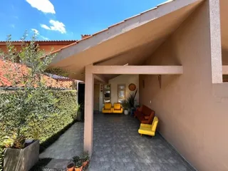Foto da fachada de uma residência com área coberta e vegetação ao ar livre.