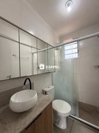 Foto interna de um banheiro com pia branca e box de vidro transparente.