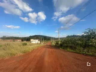Uma estrada de terra vermelha atravessa uma paisagem rural com vegetação densa.