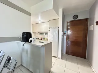 Vista interna de uma cozinha com armários brancos e eletrodomésticos.