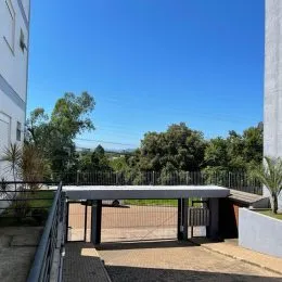 Vista externa de uma propriedade com cerca e vegetação sob um céu azul.
