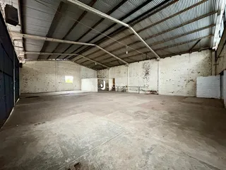 Imagem de um espaço industrial amplo com teto de metal e paredes brancas.