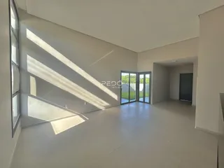 Interior de uma sala de estar ampla com piso claro e grandes janelas.