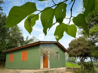 Fachada de uma casa simples verde com telhado marrom em uma área rural.