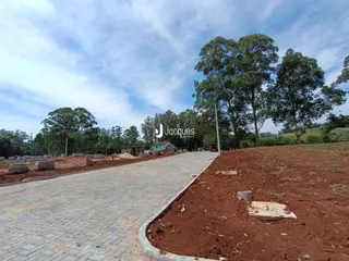 Vista externa de um terreno com área pavimentada e vegetação ao fundo.