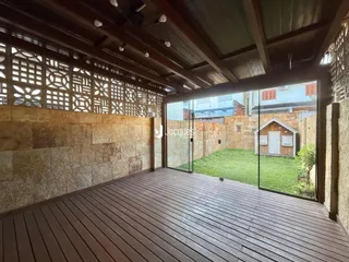Vista de uma área externa com deck de madeira e jardim de fundo.
