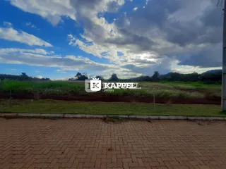 Vista panorâmica de um campo verde com vegetação ao fundo sob um céu parcialmente nublado.
