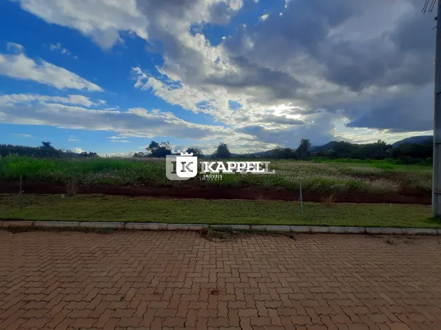 Vista panorâmica de um campo verde com vegetação ao fundo sob um céu parcialmente nublado.