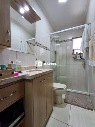 Foto interna de um banheiro com revestimento cerâmico e box de vidro.