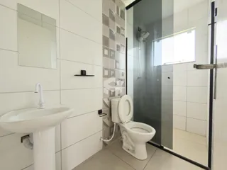 Banheiro com revestimento branco e box de vidro transparente.