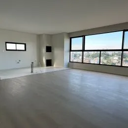 Vista interna de uma sala ampla com grandes janelas que oferecem uma vista panorâmica.