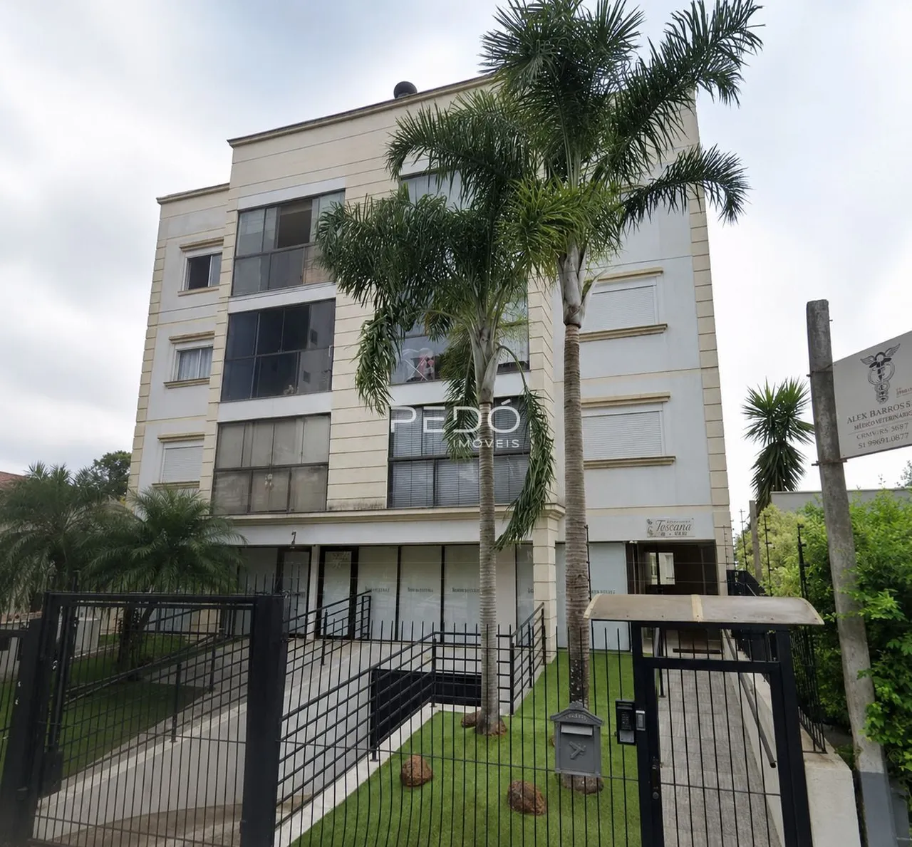 Fachada de um prédio residencial em Lajeado, Brasil, com cerca e vegetação.