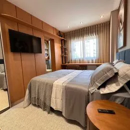 Quarto com cama e televisão montada na parede em um ambiente com painéis de madeira.