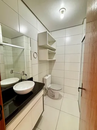Banheiro com bancada, pia e vaso sanitário em um ambiente claro com revestimento branco.
