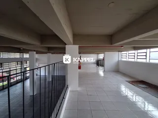 Um corredor interno com piso de cerâmica e colunas brancas em um imóvel.