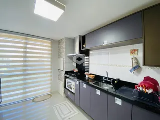 Vista interna de uma cozinha moderna com armários escuros e bancadas pretas.