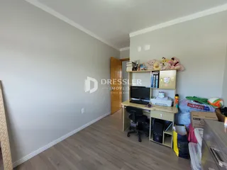 Um corredor interno com paredes cinzas e piso de madeira clara.