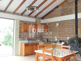 Vista interna de uma cozinha com armários de madeira e paredes de tijolo aparente.