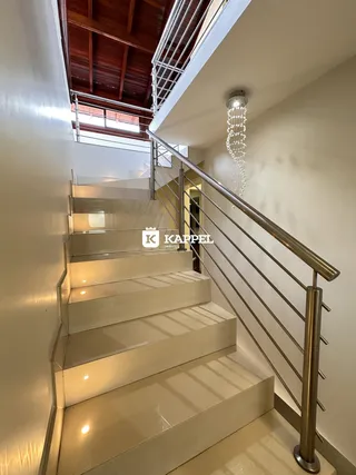 A foto mostra uma escadaria interna com degraus claros e corrimão de metal.