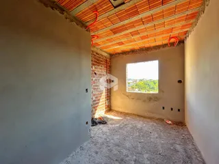 Interior de uma sala em construção com teto de telhas exposto e parede de tijolos.